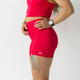 A woman wearing bright magenta legging shorts and a matching sports top, standing against a white background.
