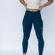 Woman wearing dark blue high-waisted gym leggings and cream racerback sports bra