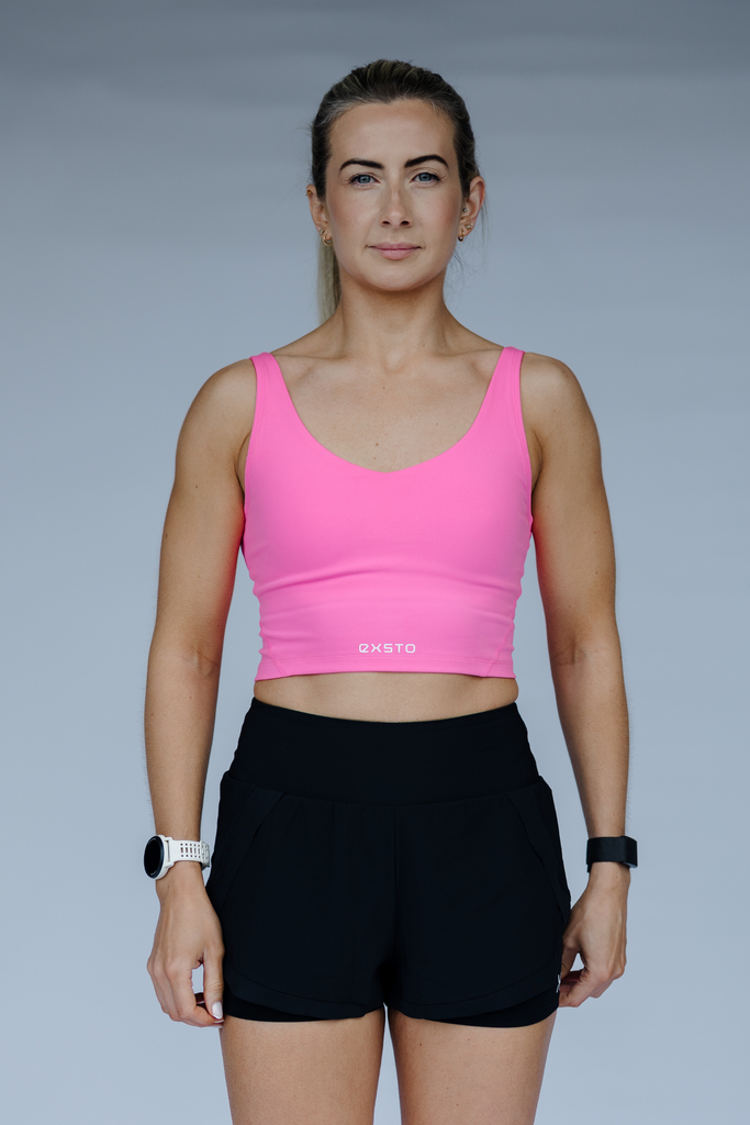 Woman wearing a pink sports bra and black shorts on a gray background