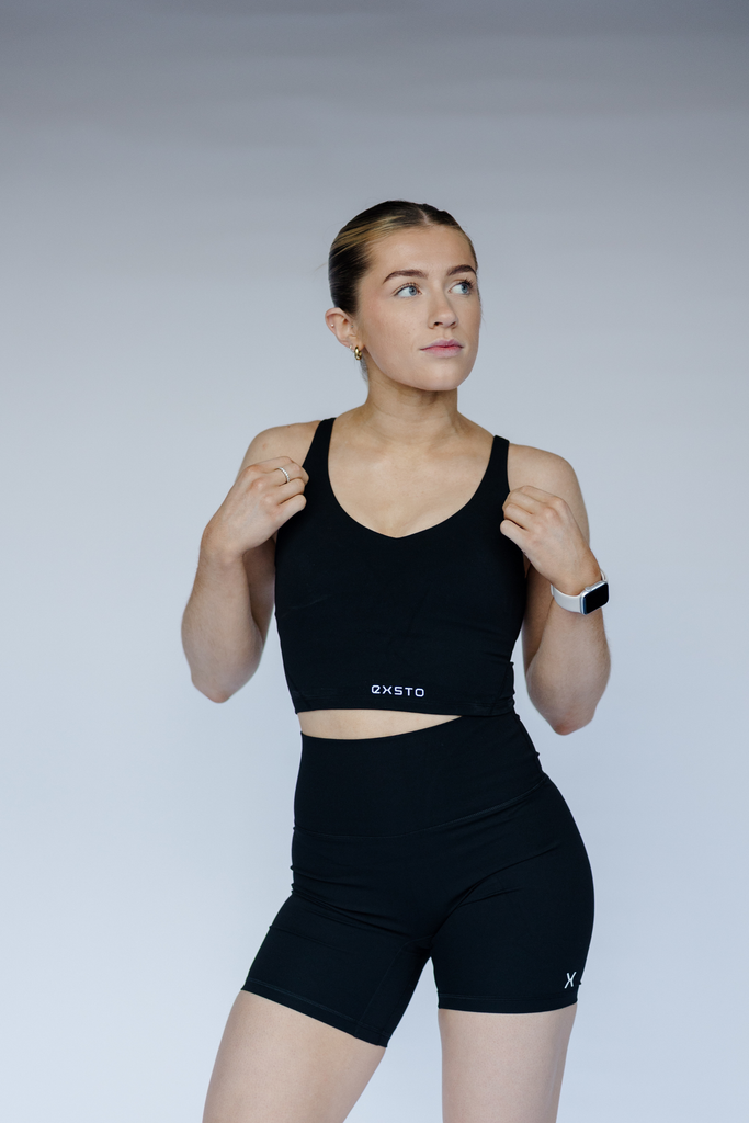 Woman wearing a black sports bra and shorts with a visible brand logo on a plain background