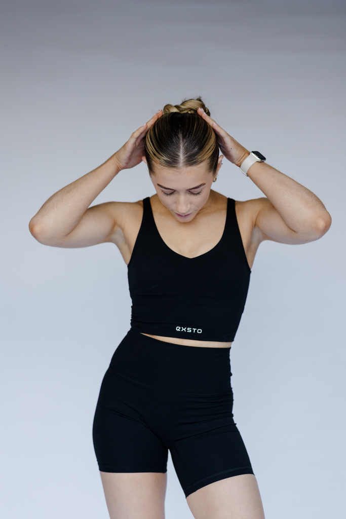 Person wearing a black sports bra and shorts with a visible brand logo on a plain background