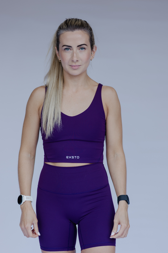 Woman wearing a purple sports outfit with 'Exsto' branding on a gray background