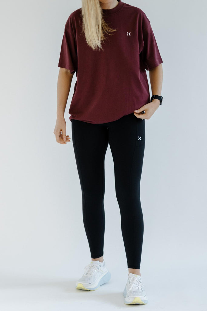 Person wearing a burgundy t-shirt and black leggings with a white logo on a plain background